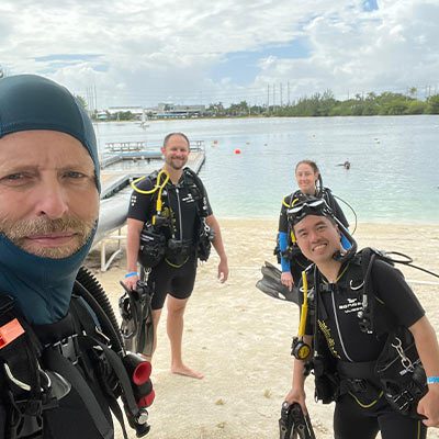 PADI-certified scuba instructors posing in full dive gear on the beach before a guided dive in Miami.