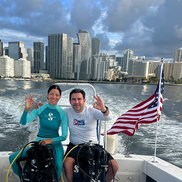 Smiling scuba divers on Miami Dive Boat with city skyline in the background, promoting certified local PADI dive charters